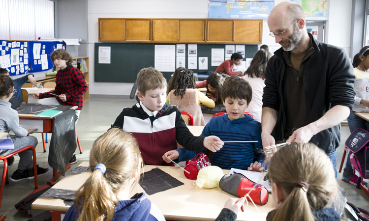 Dans la salle de classe, l'expert est à côté d'un groupe d'élèves qui commence à construire un cerf-volant.