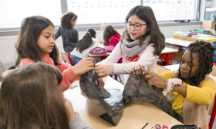 Dans une salle de classe, trois jeunes filles tiennent le bout d'un sac poubelle pour fabriquer un cerf-volant