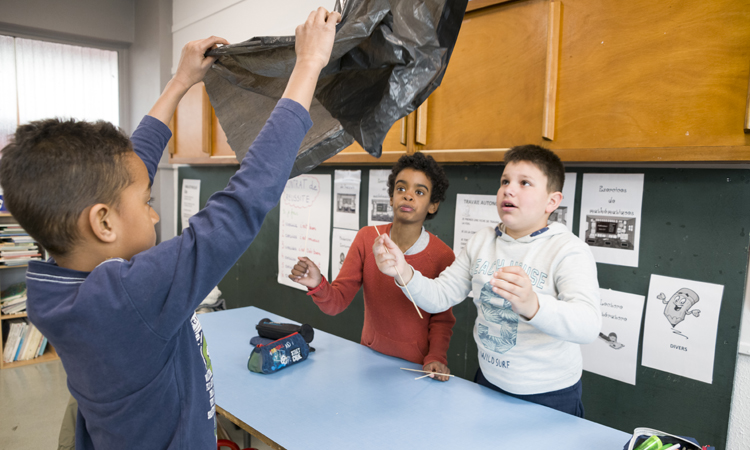Trois jeunes garçons font volet la base de leur cerf-volant dans la salle de classe