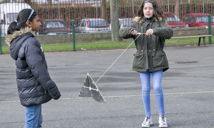 Deux petites filles font voler un cerf-volant dans la cour de l'école Guy-Môcquet
